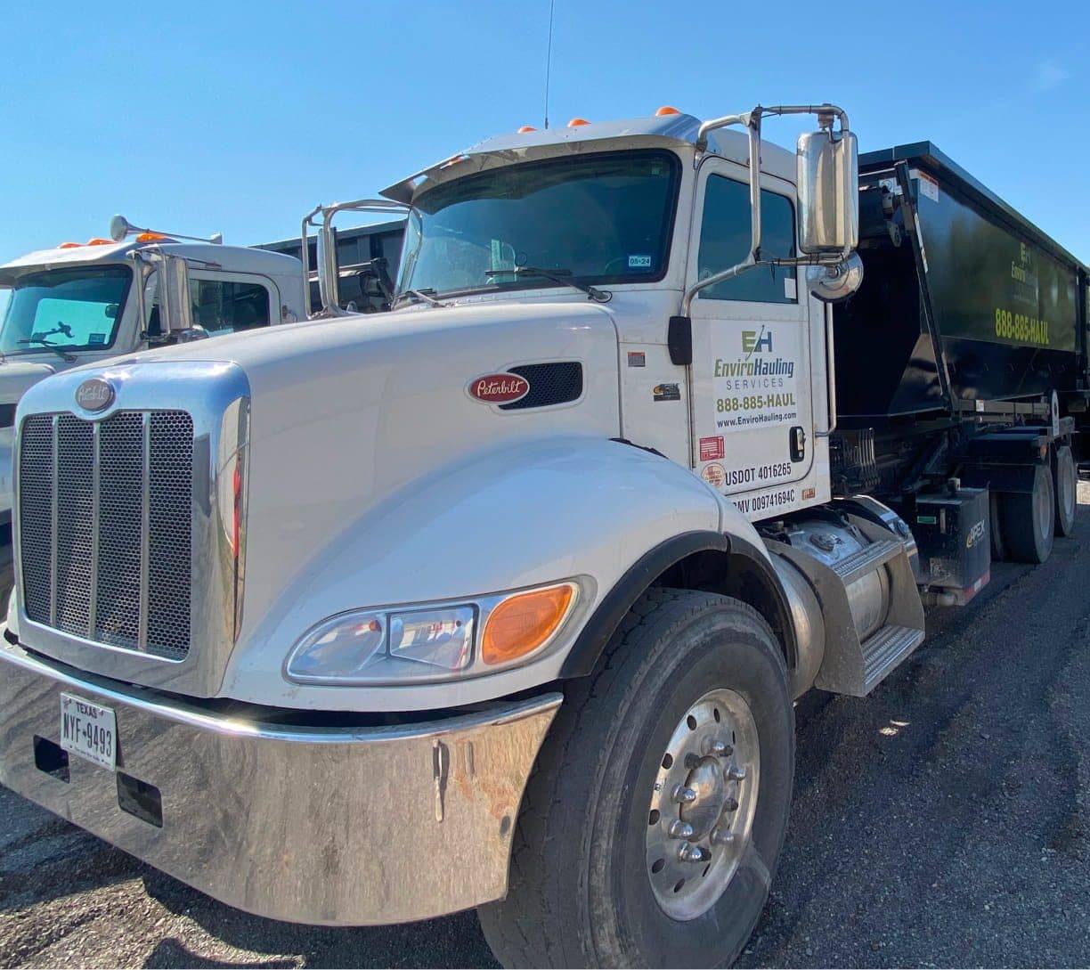 Front of a white EnviroHauling Peterbilt roll-off truck in the yard