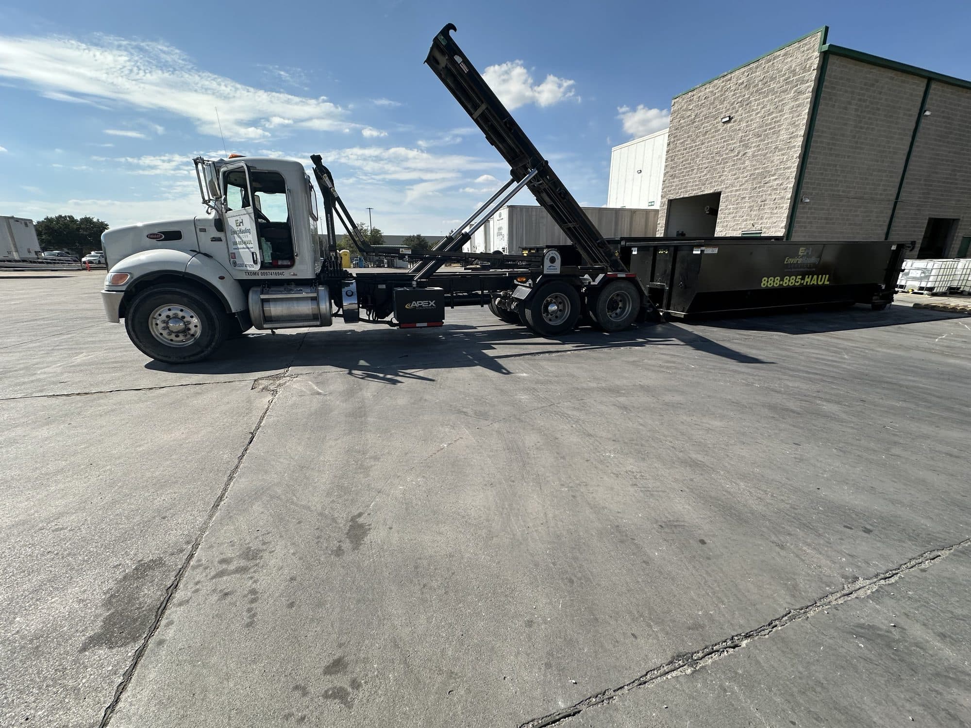 EnviroHauling hook-lift truck with a roll-off container beside a commercial building