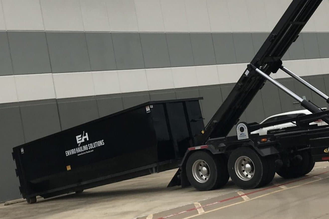 Black EnviroHauling roll-off container sliding off a hook-lift truck at a warehouse
