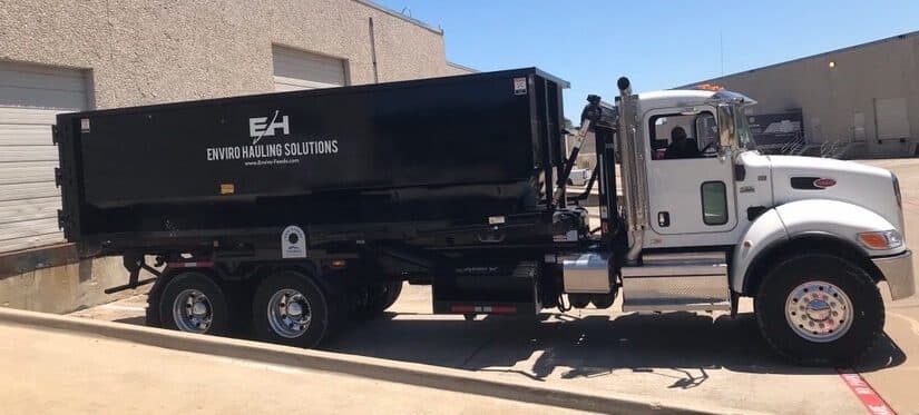 EnviroHauling roll-off truck carrying a container past a commercial building